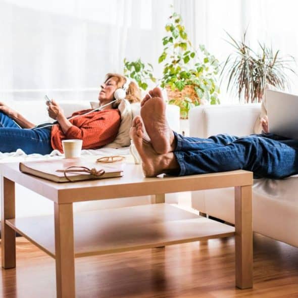A mature couple relaxes on separate couches, using their electronic devices.