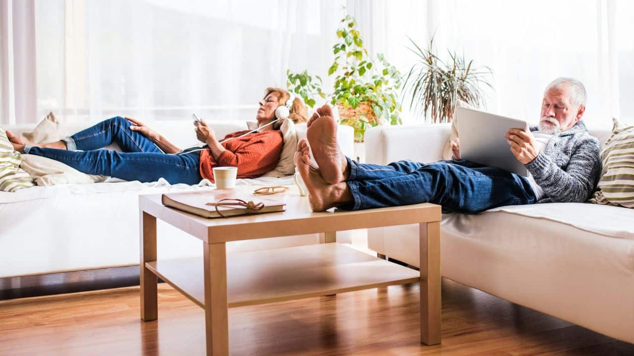 A mature couple relaxes on separate couches, using their electronic devices.