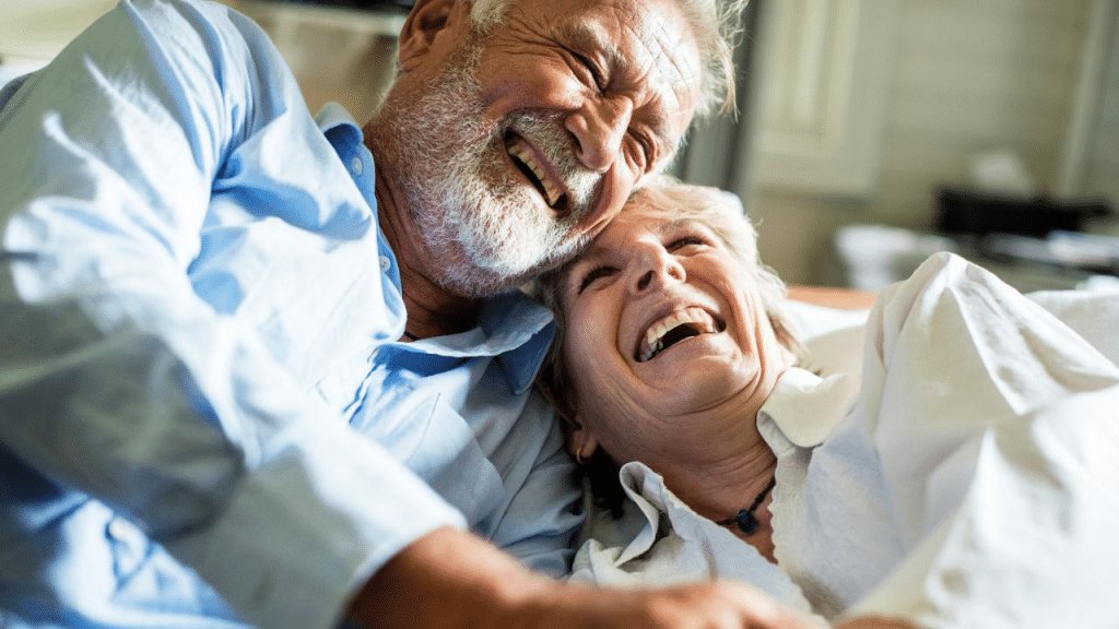A joyful, elderly couple with white hair and big smiles embraces each other while laughing.