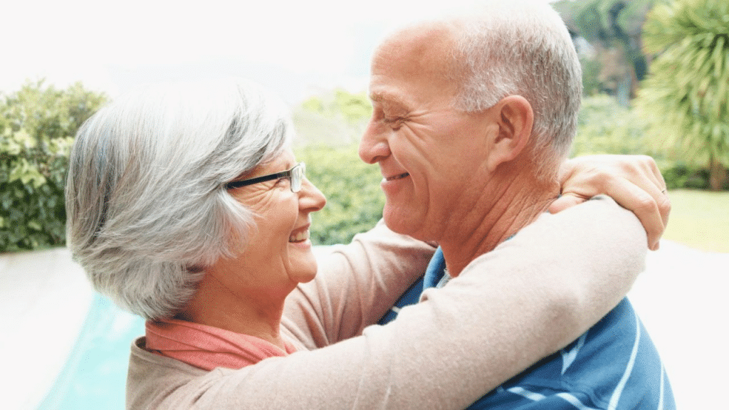 A joyful, older couple with white hair hugs while looking at each other.