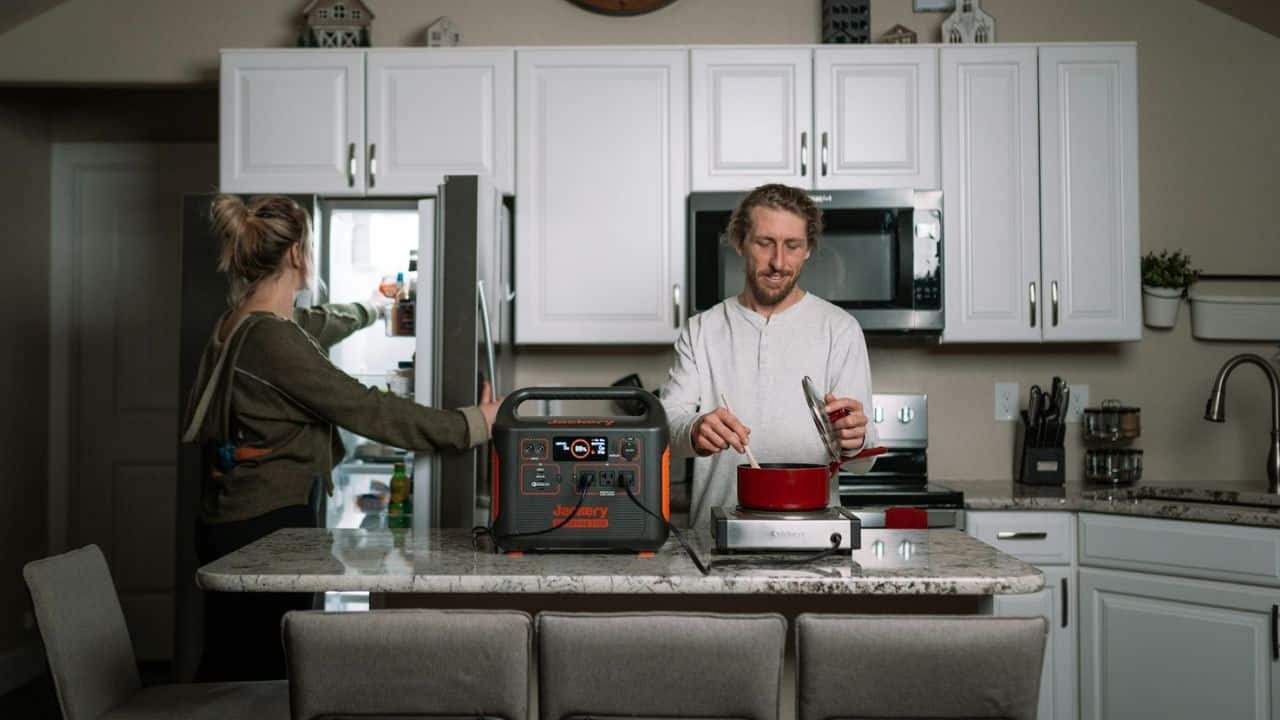 A woman looks inside a refrigerator as a man stirs a pot on a counter in a kitchen.