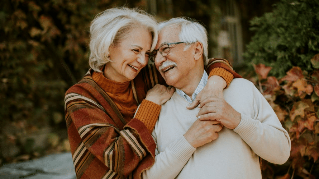 A joyful, elderly couple hugs, smiling and looking into each other's eyes.