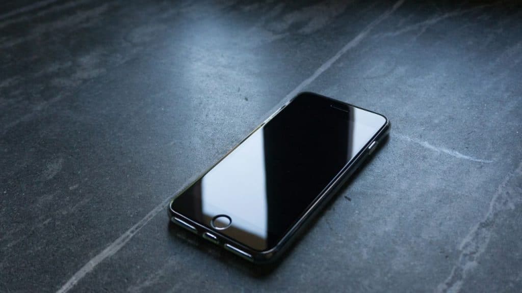 A smartphone with a blank, dark screen is placed on a marbled, dark grey surface.