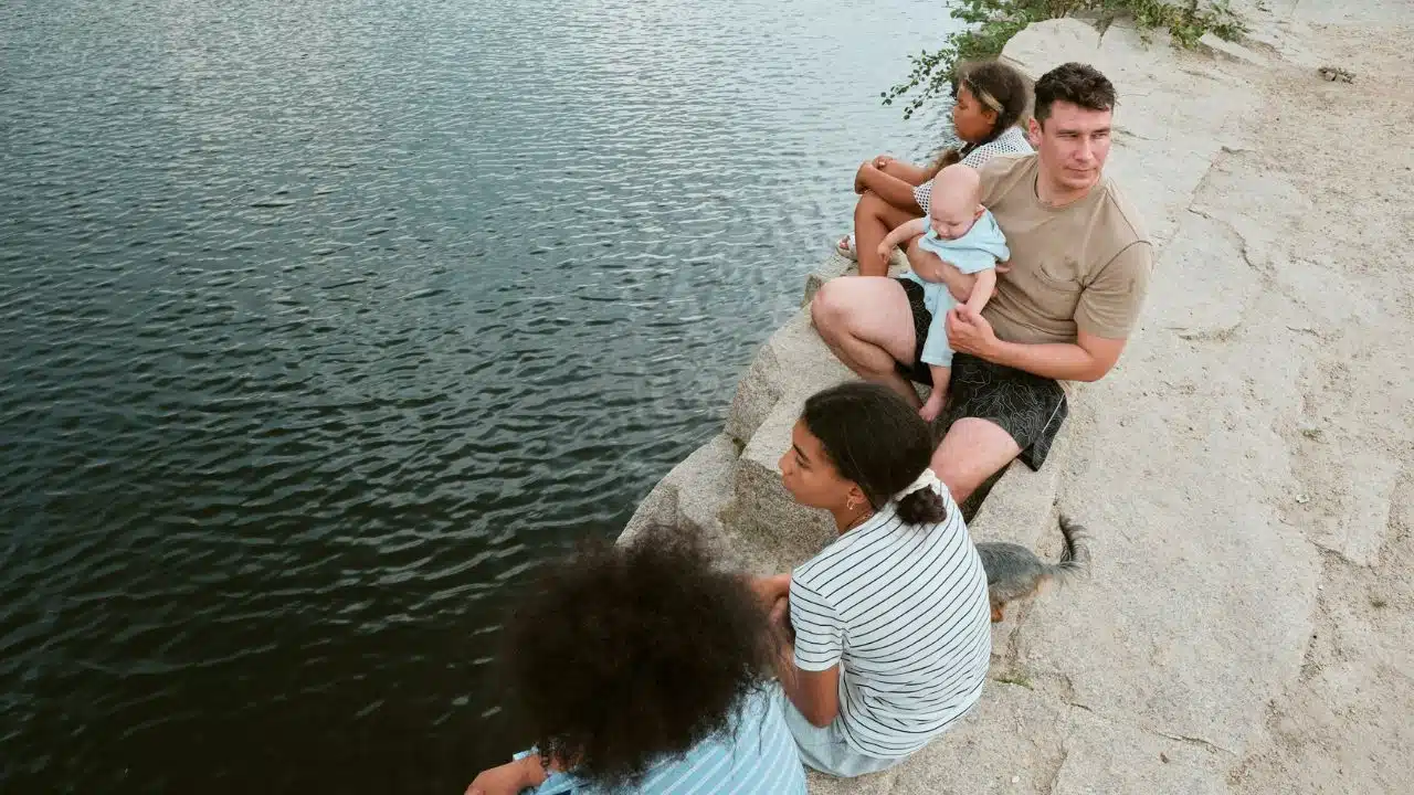 A father and three children are sitting on rocks next to a body of water.