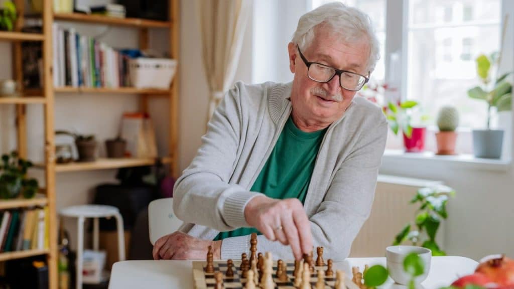 A cheerful older man with glasses is playing a game of chess.