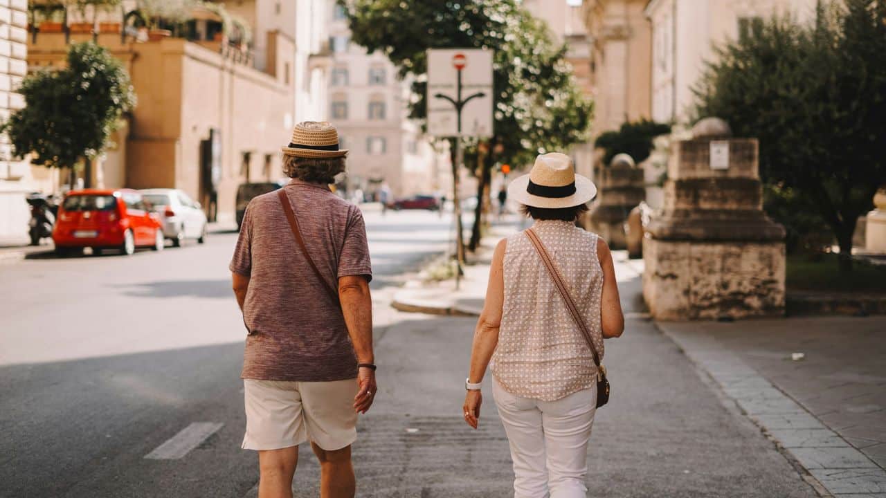 A man and a woman in straw hats walk down a city street, seen from behind.