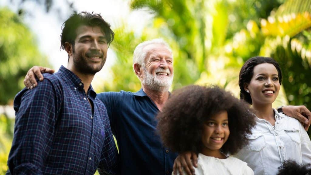 A multi-generational and diverse family is standing outdoors and smiling together.