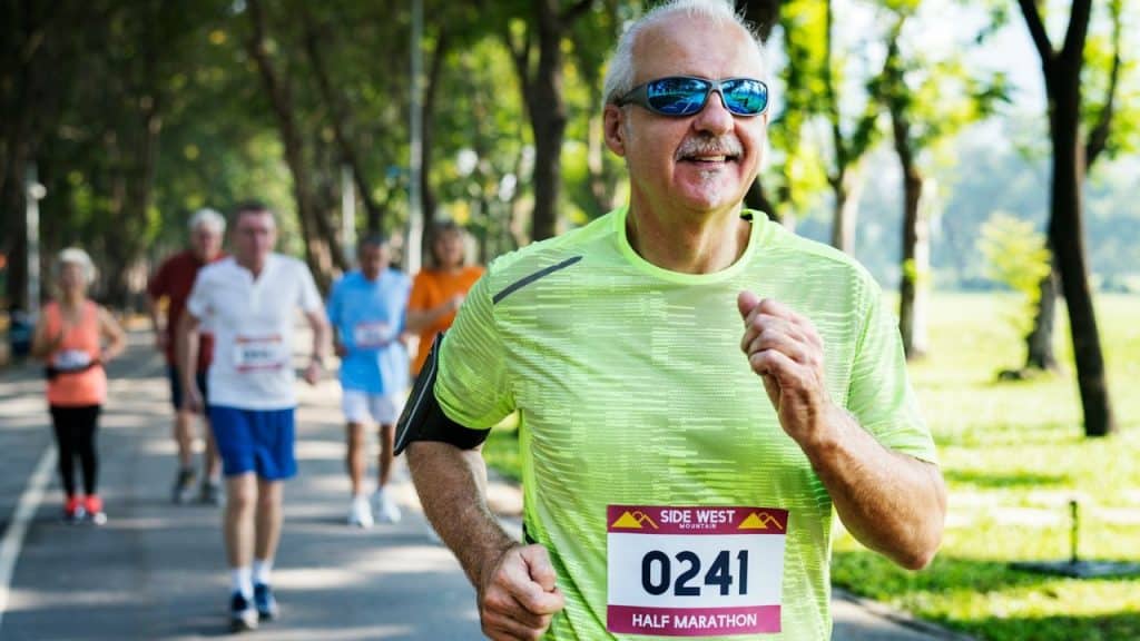 A cheerful older man with a mustache and sunglasses is running in a half marathon.