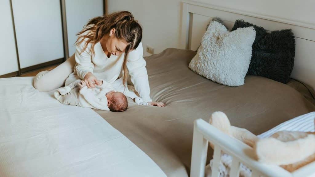 A mother in white clothes cares for her baby on a bed.