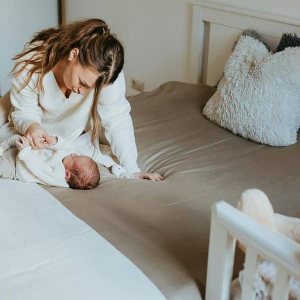 A mother in white clothes cares for her baby on a bed.