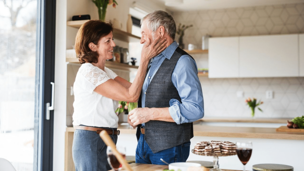 A happy, older woman wearing a white shirt lovingly touches the face of a smiling, older man.