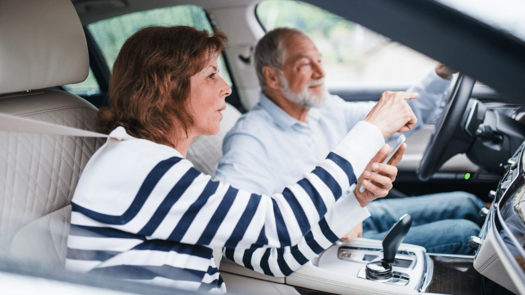 A gray-haired couple in a car looks at a map on a phone while the man is driving.