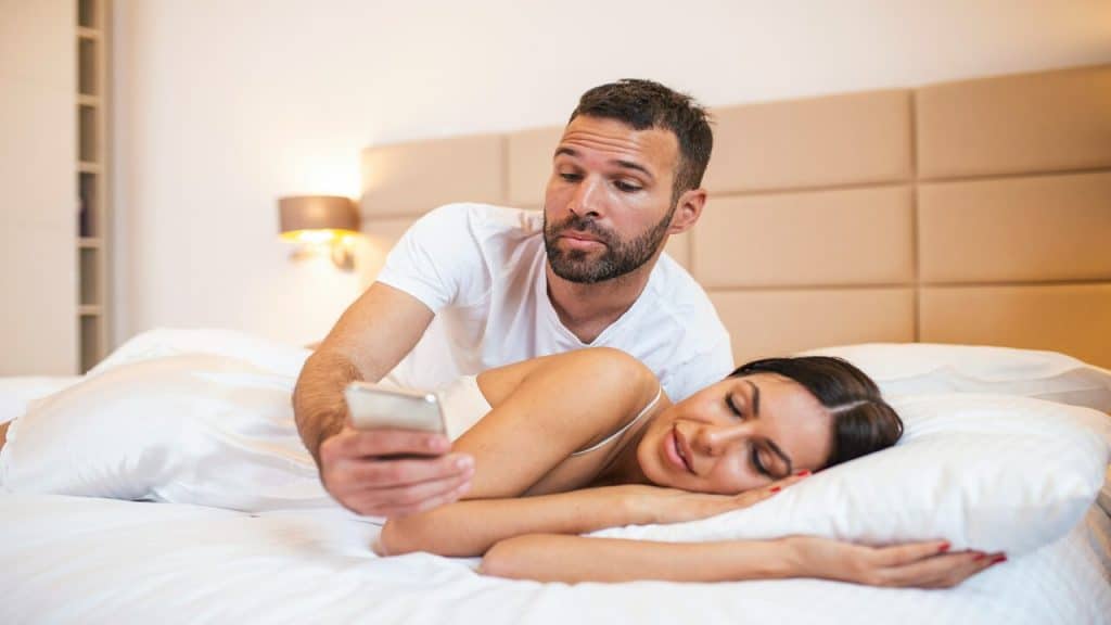 A man checking his wife’s phone while she sleeps