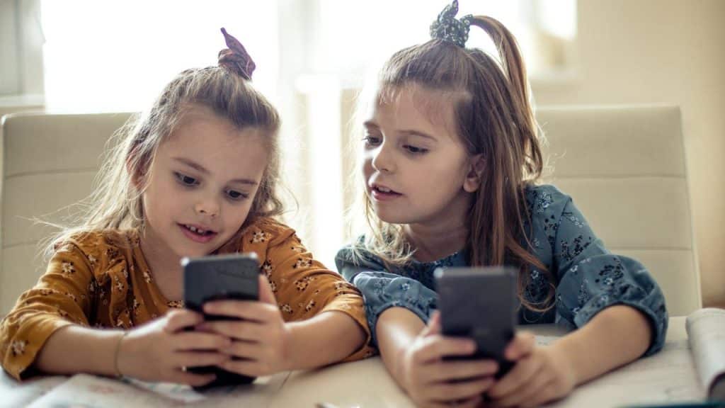A pair of young girls look at smartphones together.