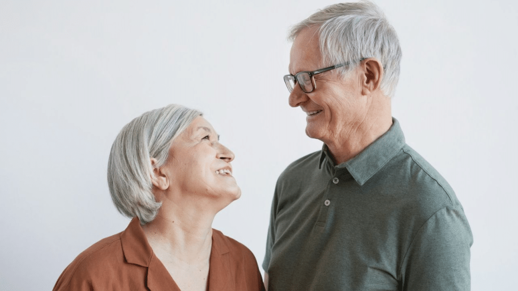 A joyful elderly couple with gray hair looks at each other while smiling.