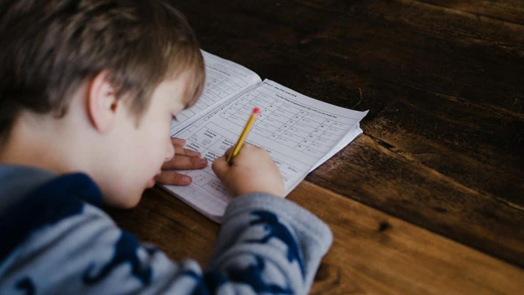 A child writes in a workbook with a pencil.