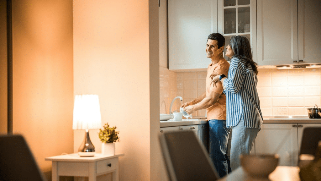 A middle-aged couple smiles while washing dishes together in a modern kitchen.