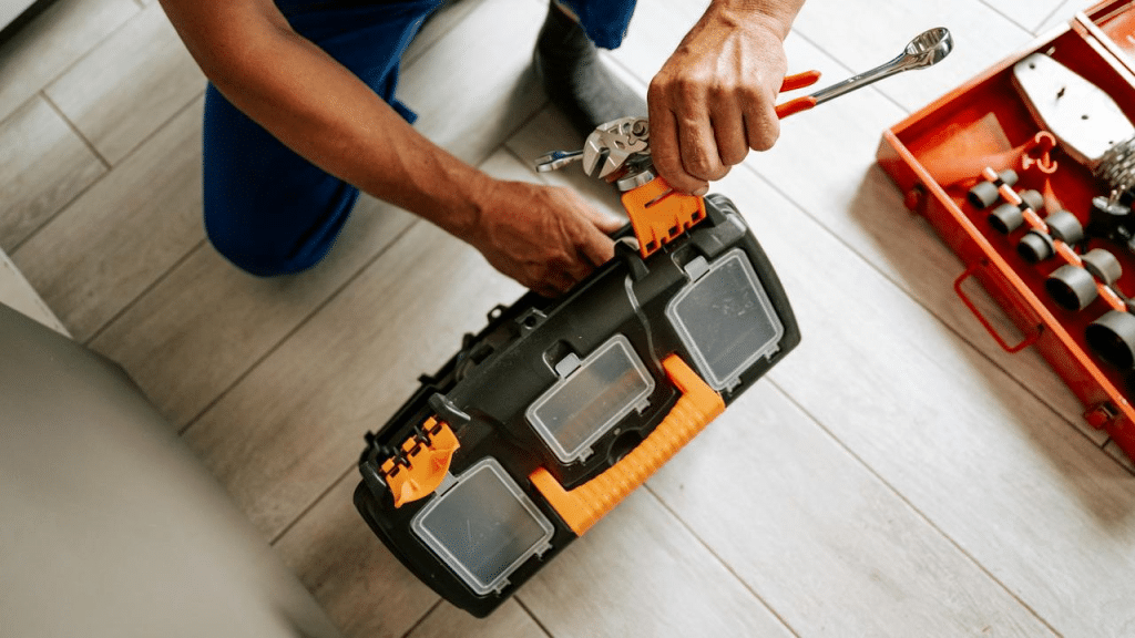 A person holding a toolbox and tools on the floor.