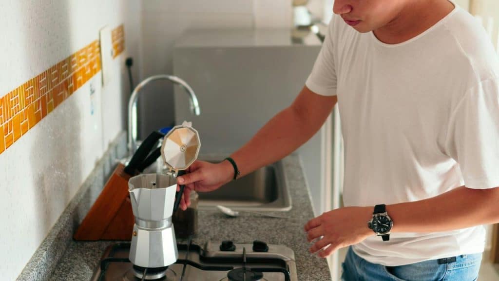 A man making coffee using a stovetop espresso maker in the kitchen.