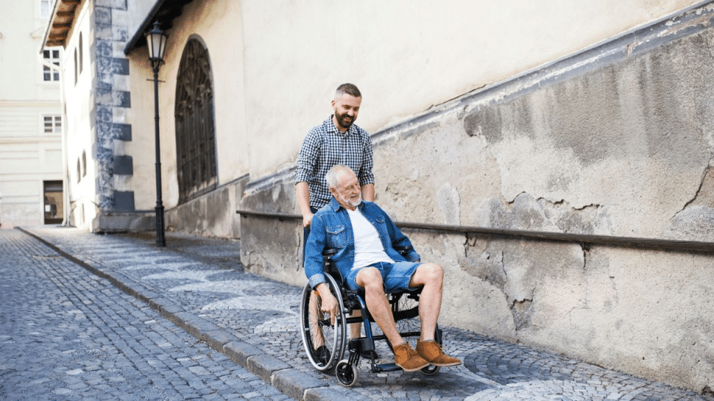 A man pushes an older man in a wheelchair on a cobblestone street.