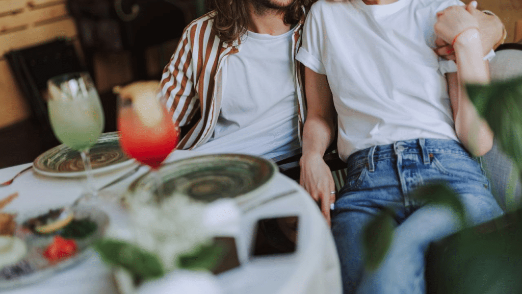 A couple sits closely together at a table with drinks and plates.