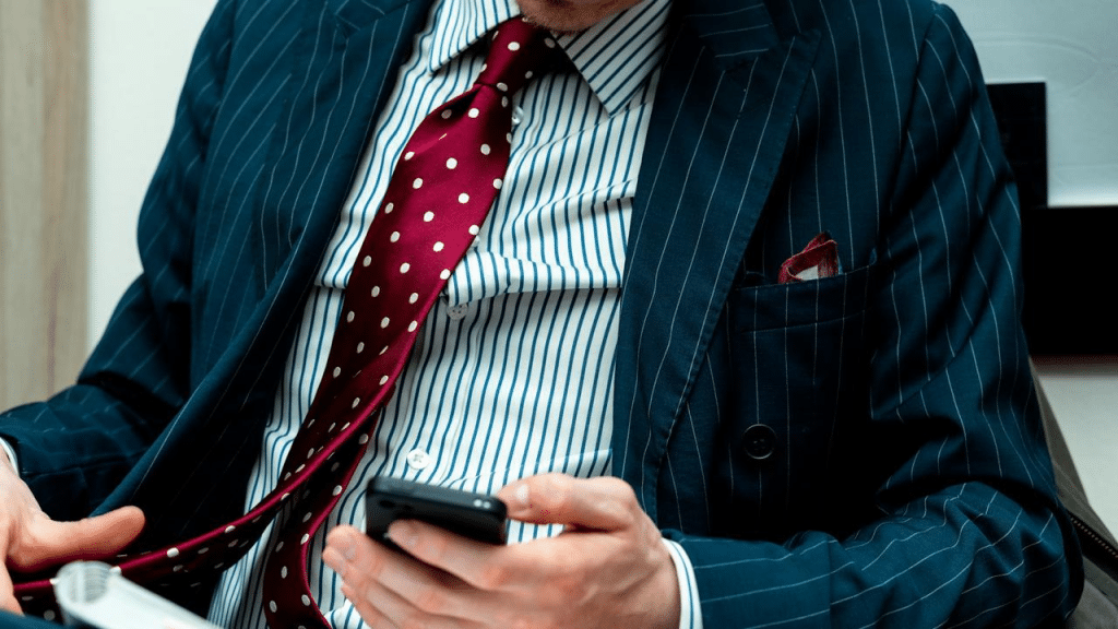 A man in a pinstripe suit with a red polka dot tie holding a smartphone.