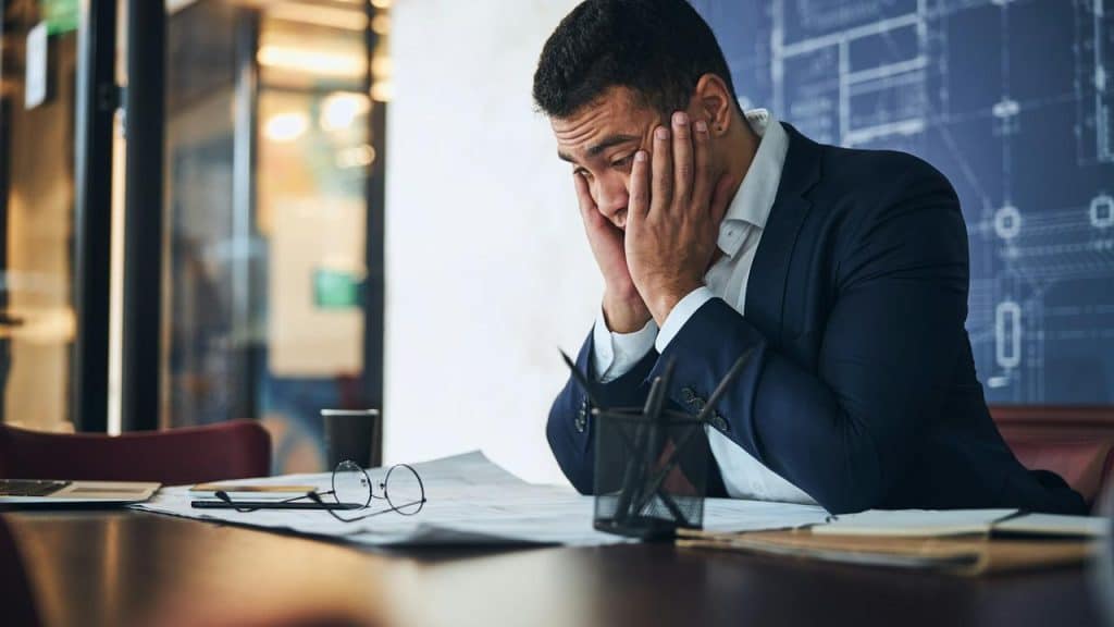 A stressed businessman sitting at a desk with papers.