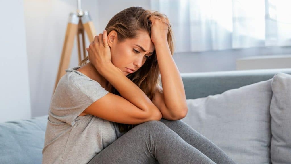A dejected woman sits on a couch with her head in her hands.
