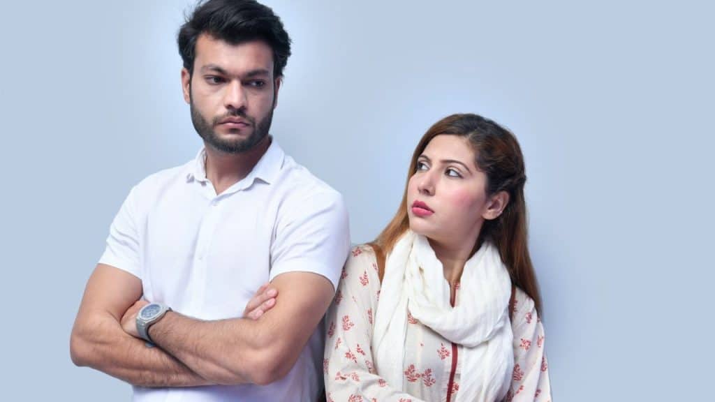 A serious man with crossed arms looks away from a woman looking at him.