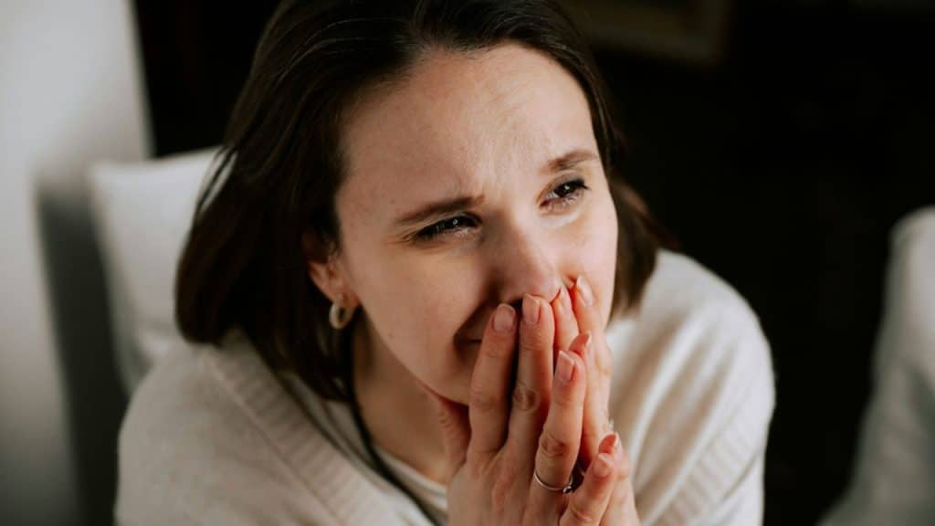 A sad woman covers her mouth with her hands, looking down and away.