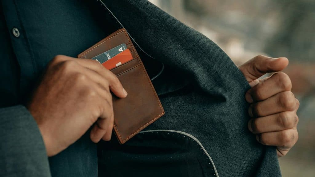 A person in a suit jacket slips a brown leather wallet into their inner pocket.
