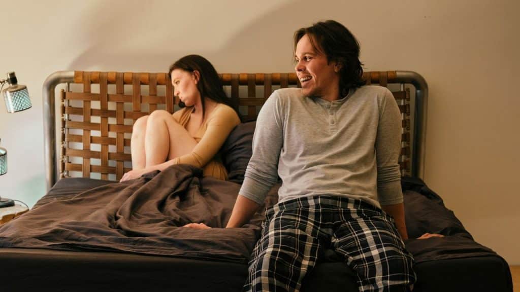 A woman sits with her back to a man who is smiling and laughing on a bed.