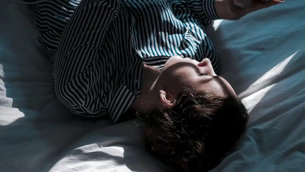 A woman lying on a bed in sunlight.