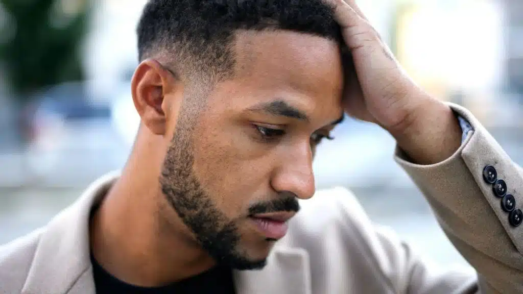 A worried man in a beige blazer holds his head and looks down.