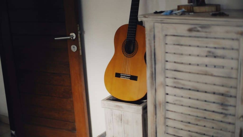 Acoustic guitar rests against a wall next to a wooden cabinet.