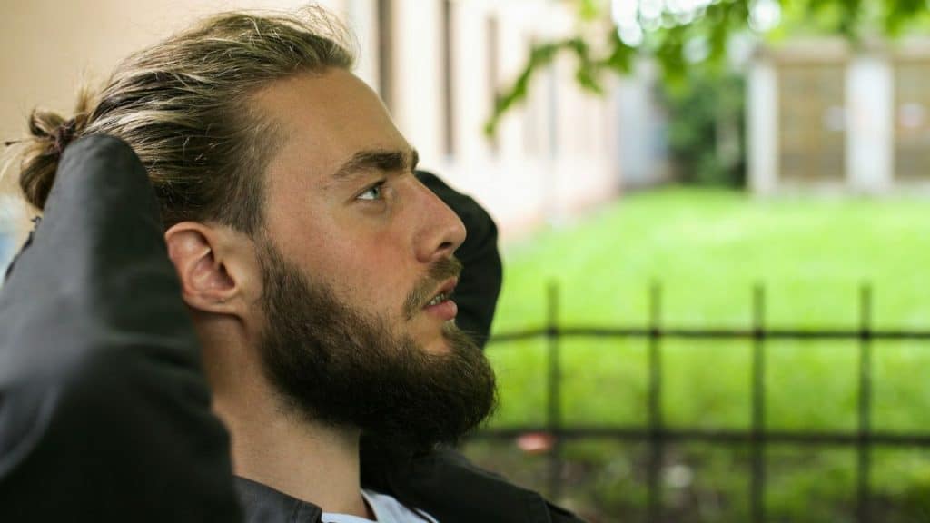 A pensive, bearded man in a leather jacket looks away from the camera.