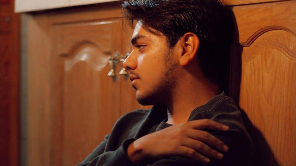 A thoughtful young man with his arms crossed looks away from the camera.