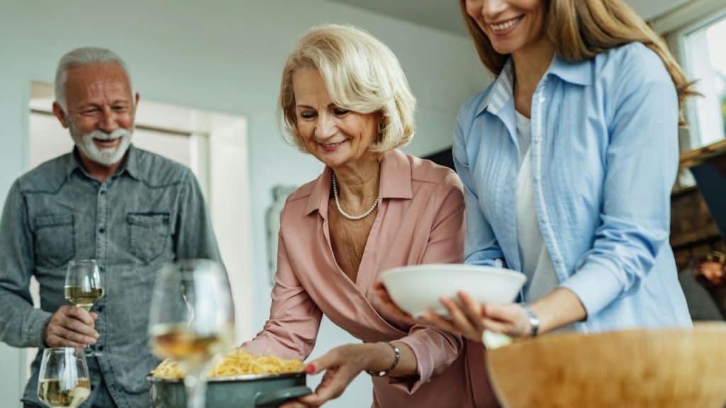 A family standing together around a table, serving food and holding glasses of white wine.