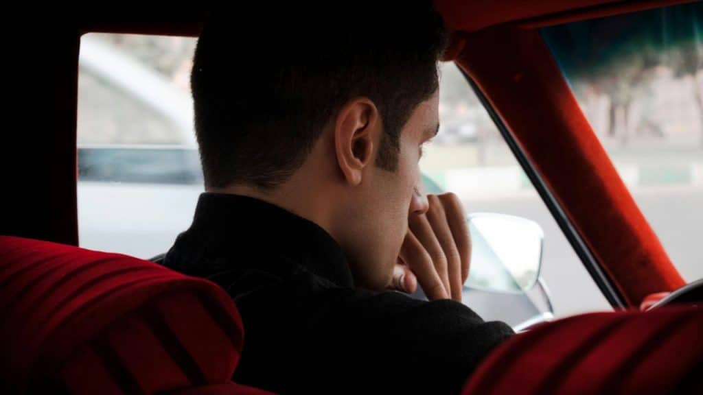 A man in a car, seen from behind, looking out the window.