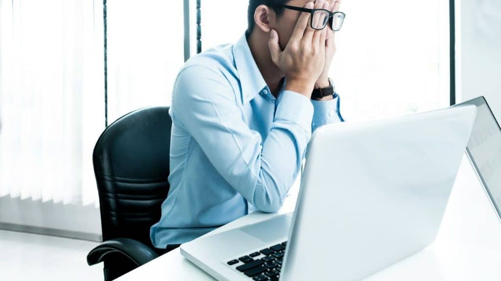 A stressed man at a desk with his hands covering his face.