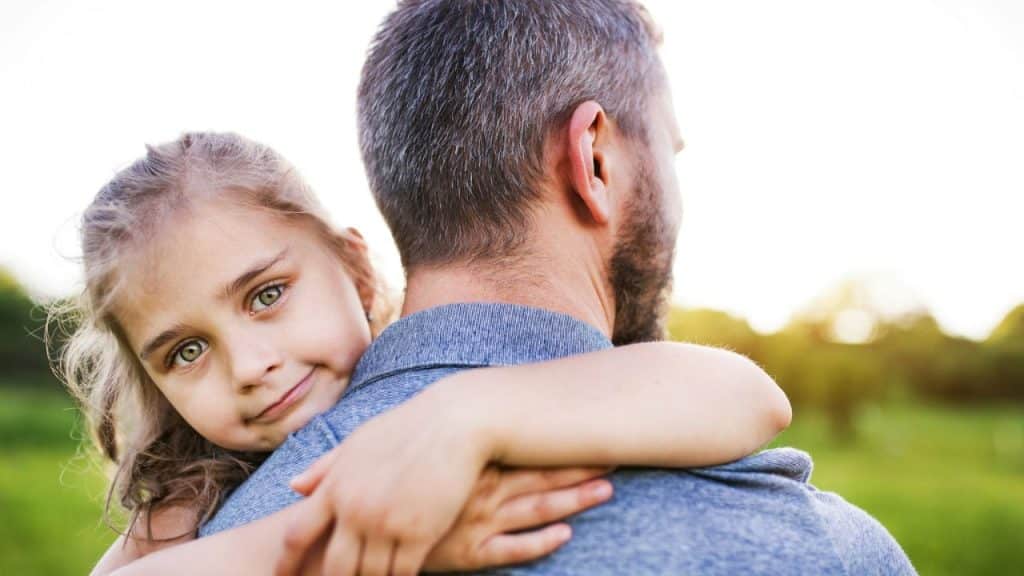 A smiling girl with green eyes looks over her father's shoulder.