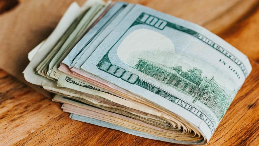 A stack of US dollar bills on a wooden surface.
