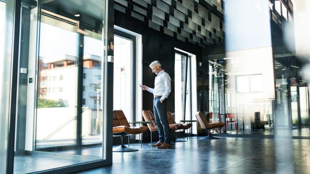 A man standing in a modern office looking at his phone.