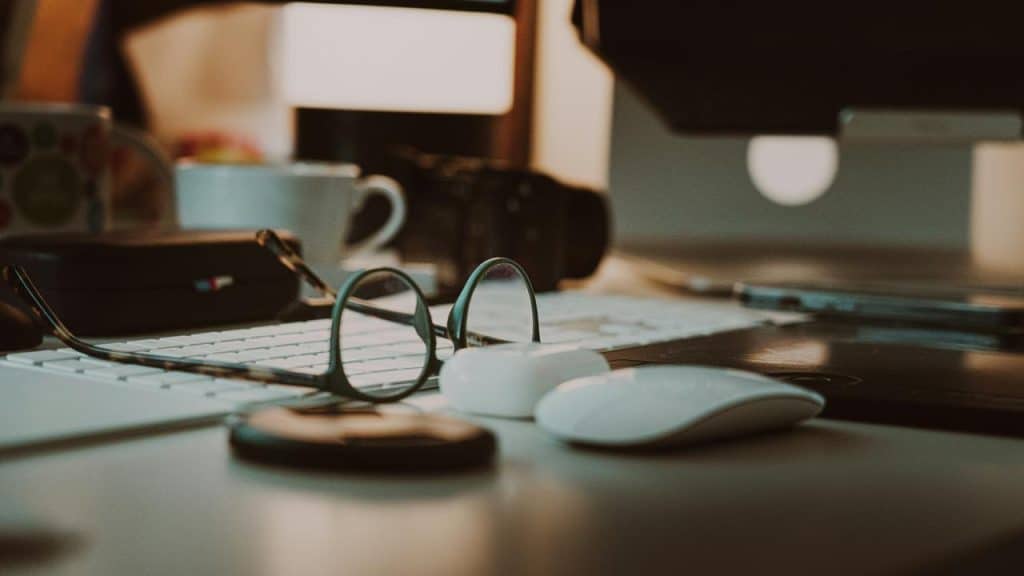 A close-up of a cluttered desk with glasses, a keyboard, and a computer mouse.