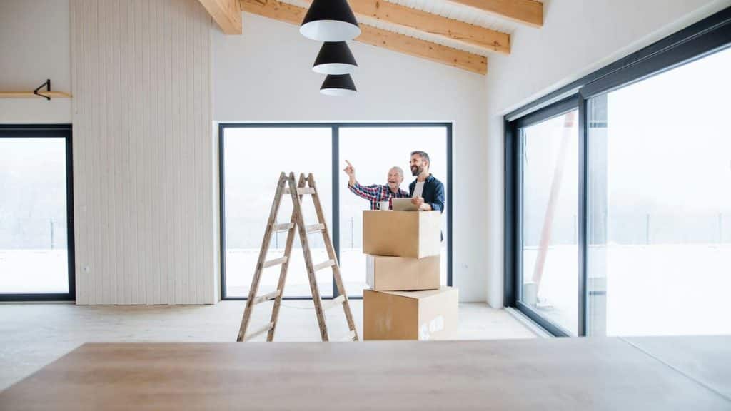 A photo of two men standing inside a new home with moving boxes and a ladder.