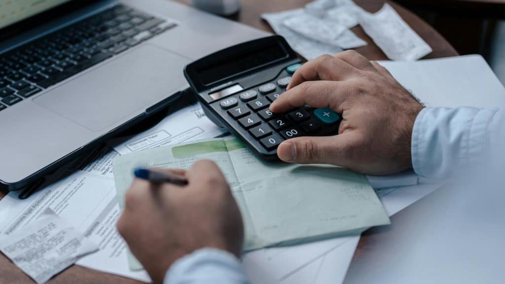 A person using a calculator and writing while working on financial documents.