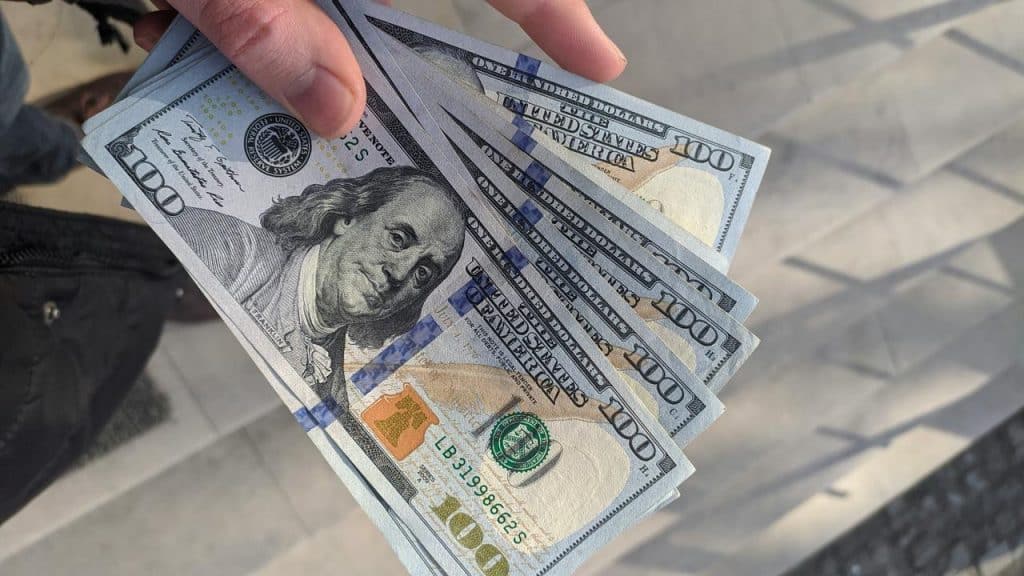 A person’s hand holding several one-hundred-dollar bills.