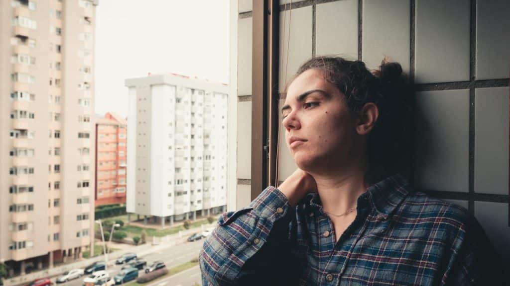 A woman leaning against a wall looking out the window.