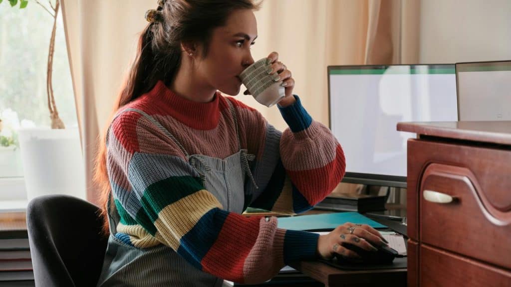 A woman drinking coffee while working at a computer.