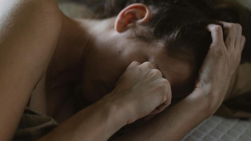 A woman lying in bed covering her face with her hand.